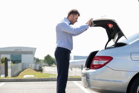 Handsome businessman is preparing for flight in the airport. He is picking up a suitcase from a luggage carrier of his car. He is looking at it seriously. Copy space in left sideの写真素材