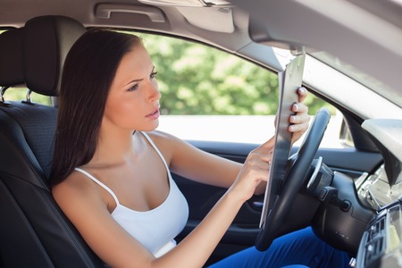 Pretty girl is sitting at the steering wheel of new car. She is reading documents concerning its selling. The lady is looking at it with seriousness and concentrationの写真素材