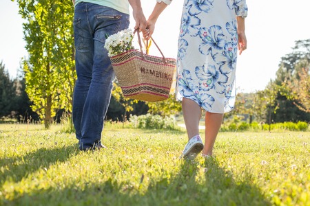 Close up of legs of loving couple carrying a basket with flowers together. They are dating in the natureの写真素材