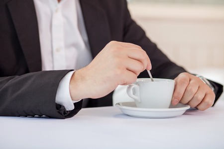 Close up of hands of man drinking coffee. He is sitting and the table in suitの写真素材