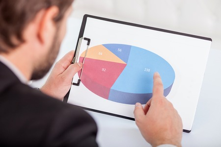 Close-up of male hands holding sketches of new project. The man is pointing his finger at the diagram.  He is looking at these papers with concentrationの写真素材