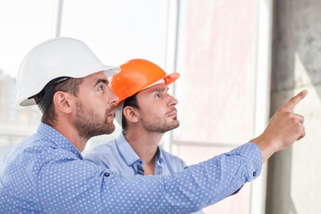 Attractive architect is explaining to a foreman the main concepts of construction. He is pointing...