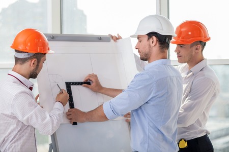 Handsome architect and his colleagues are drawing sketches of building. They are taking measurements...