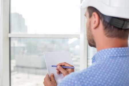 Cheerful engineer is looking through the window. He is designing the plan of new building with concentration. Focus on his back. Copy space in left sideの写真素材