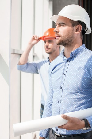 Cheerful architect and attractive foreman are looking through the window with aspirations. They are planning to build a new constructionの写真素材