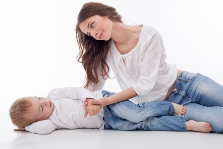 Pretty woman is lying near her son. They are holding hands and looking at each other with gentleness. Isolated on backgroundの写真素材