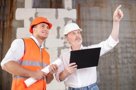 Experienced old architect is explaining to the foreman his ideas about building. He is pointing his...