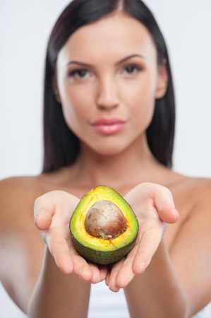 Beautiful woman is presenting an avocado. She is holding it in her palms. She is looking at the camera with confidence. Focus on avocado and isolatedの写真素材