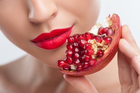 Close up of pretty woman showing a slice of pomegranate to the camera. She is gently smilingの写真素材