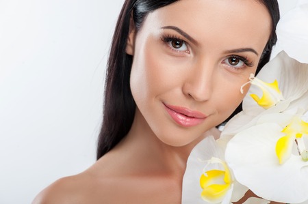 Cheerful girl is holding a bucket of white flowers. She is touching it to her body gently. The lady is looking at the camera with enjoyment and smiling. Isolated and copy space in left sideの写真素材
