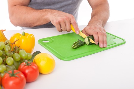 Close up of male hands cutting a cucumber on the desk. There are abundance of fruits and vegetables on the tableの写真素材