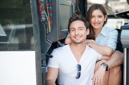 Beautiful woman and man are sitting on the steps in doors of the bus. They are waiting for beginning of their journey with anticipation. The lovers are embracing and smilingの写真素材