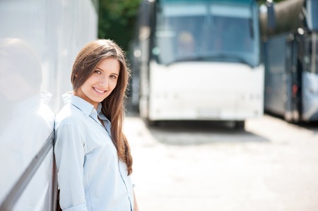 Attractive woman is leaning on the bus. She is waiting for bus departure with anticipation. The lady is smiling and looking forward with pleasure. Copy space in right sideの写真素材
