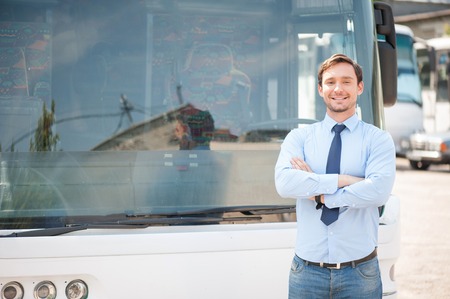 Handsome man is standing near a bus. He is looking at the camera with joy and smiling. The man crossed his handsの写真素材