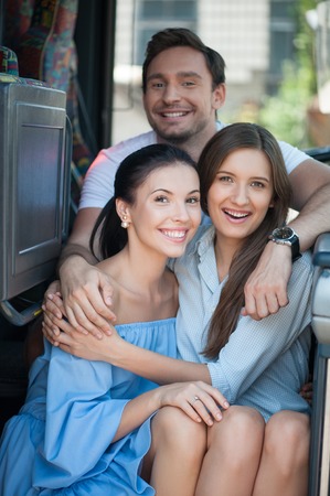 Attractive women and handsome man are making their journey together. They are sitting on the doorsteps of the bus and embracing. They are smiling and looking forward with joyの写真素材