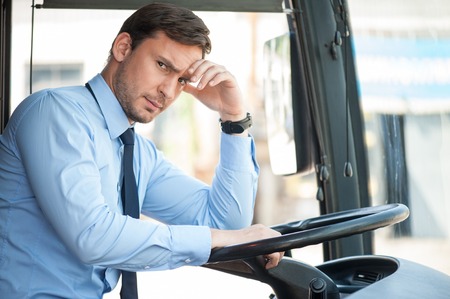 Cheerful man is driving a bus. He is touching his forehead. The man has a headache. He is looking at the camera with frustrationの写真素材