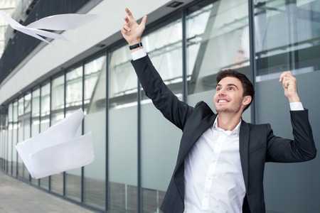 Cheerful businessman is throwing papers with happiness. The deal was done successfully. The man is smiling and gesturing positivelyの写真素材