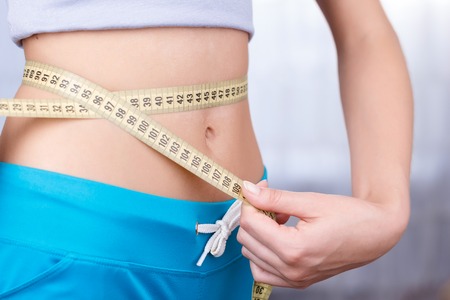 Slim and beautiful. Slim girl wearing blue shorts and holding yellow measure tape while measuring...