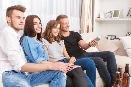 Time to relax. Pleasant cheerful friend sitting on the couch and watching TV while having fun...
