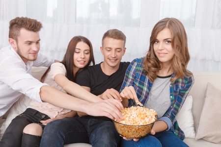 Share with me.  Pleasant contented friends eating popcorn and sitting on the sofa while feeling delightedの写真素材
