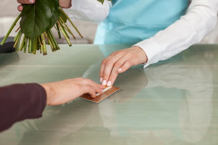 Close up of hands of florist selling flowers to her customer. She is holding a bouquet and receiving a credit card from a womanの写真素材