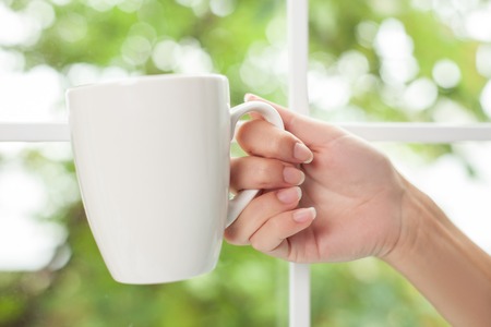 Close up of female arm holding a white cup. The girl is drinking coffeeの写真素材
