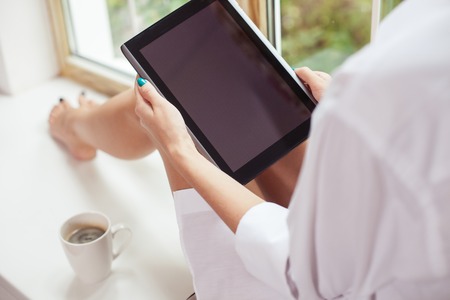 Close up of female body sitting near a window. The girl is using a laptop and drinking coffee with enjoymentの写真素材