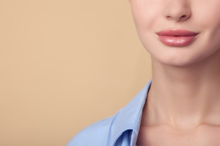 Close up of female lower half of face and neck. The girl is smiling. Isolated on brown background and copy space in left sideの写真素材