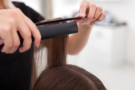Close up of arms of hairstylist equalizing female hair. The woman is holding a comb and hair ironの写真素材