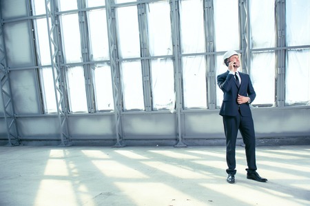 Attractive engineer is standing in a large empty building and smiling. He is looking around and talking on the phone with his customer. His project was approved. Copy space in left sideの写真素材