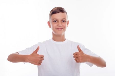 Pretty male teenager is giving thumb up with both his hands. He is smiling and looking at the camera happily. The boy is standing in a white t-shirt. Isolated on backgroundの写真素材