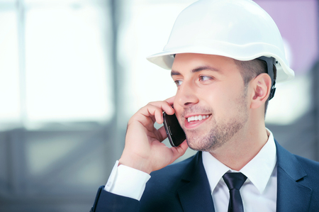 Successful architect is talking on the mobile phone with his client. He is looking aside and smiling. The customer approved his plan of building. Copy space in left sideの写真素材