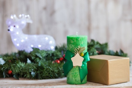 Christmas wreath of fir tree is lying on wood surface. There are toy bear, candle and golden box of gift near itの写真素材
