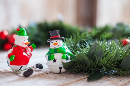 Marry Christmas. Cheerful two toy snowmen are standing on white wood surface near pine garlandの写真素材