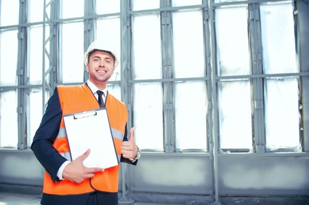 Handsome architect is standing and holding a folder of documents. He is showing paper to the camera...