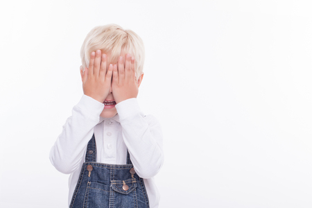 Cheerful boy is standing and covering his eyes with his arms. He is smiling shyly. The boy is expecting a big surprise. Isolated and copy space in right sideの写真素材