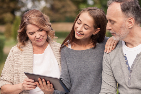 Pretty old married couple and their young daughter are using a tablet. They are looking at it with...