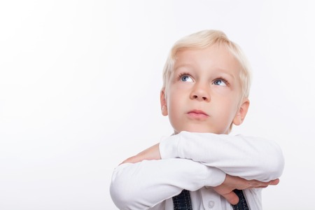 Cute boy is standing and dreaming. He crosses his hand and leaning his head on it. The boy is looking up pensively. Isolated and copy space in left sideの写真素材