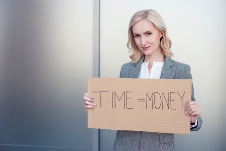 Time is money. Successful woman in formalwear is standing and holding a billboard. She is looking forward confidently and smiling. Copy space in left sideの写真素材