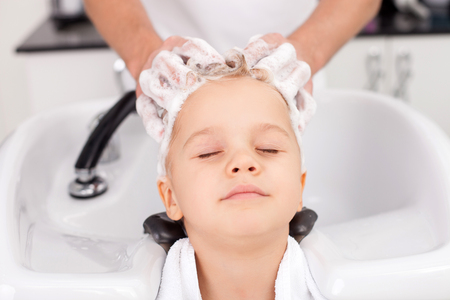 Close up of male arms of beautician. The man is standing and washing head of boy with shampoo. The kid closed his eyes with enjoymentの写真素材