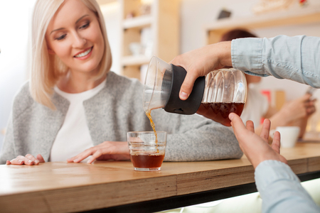 Close up of male hands of coffee maker serving customer in cafeteria. The man is pouring coffee into cup carefully. The woman is looking at hot drink and smilingの写真素材