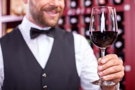 Close up of hands of professional sommelier. He is holding a glass of red wine and smiling. Focus on alcohol drinkの写真素材