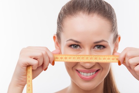 Beautiful healthy slim woman is holding tape-line near her face. She is standing and smiling. The lady is looking at camera with joy. Isolatedの写真素材
