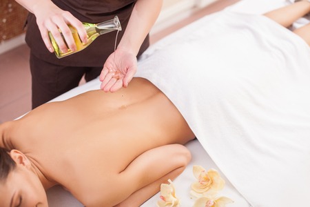 Close up of female hands of masseuse serving her client. She is standing and holding bottle of massage oil. The woman is pouring substance into hands.の写真素材