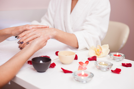 Close up of arms of young masseuse sitting at table and serving customer at spa. The woman is massaging female hand and applying moisturizing cream on it.の写真素材
