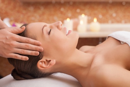 Beautiful young woman is getting head massage at spa. She is lying and smiling.の写真素材