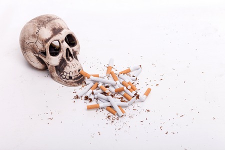 Smoking is death. Close up of heap of broken cigarettes near skull. Isolatedの写真素材