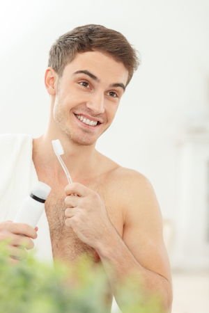 Handsome young man is brushing his teeth in the morning. He is standing and smiling. The man holding a tooth-brush and tooth-pasteの写真素材