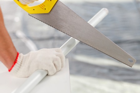 Close up of hands of builder sawing a stick. The man is holding metal sawの写真素材