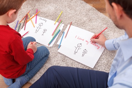 I love my daddy. Pretty father and his child are drawing pictures of their family. They are sitting on flooring with joyの写真素材